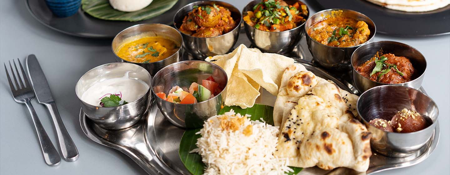Naan, curries and gulab jamun served on a steel thali